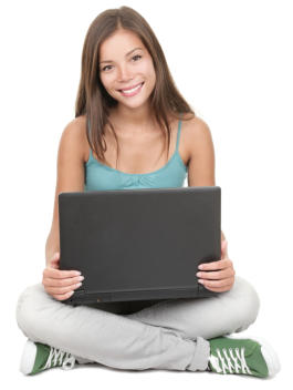 A young woman sits cross legged on the floor with a laptop in her lap. She is looking at the camera and smiling.