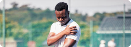 A young man on a tennis court holds a tennis racquet and grips his shoulder in pain